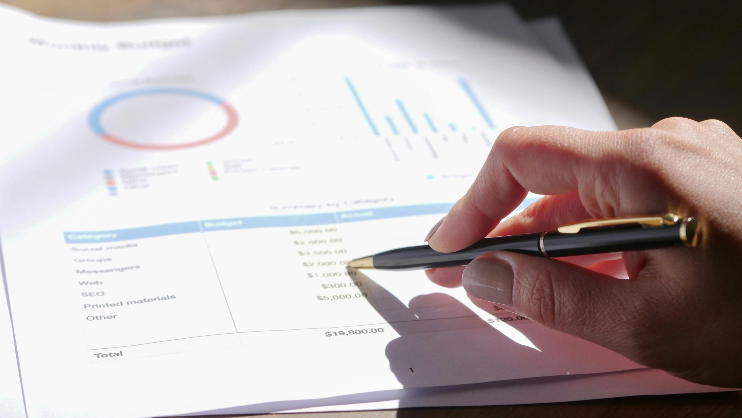 Hand pointing a pen at a paper containing financial reports